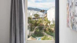 Un dormitorio con cama, ventana con vistas a edificios y una piscina, y un cuadro en la pared.