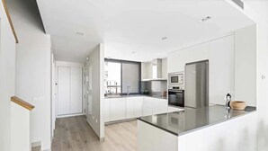 Una cocina moderna con armarios blancos, una isla central, electrodomésticos de acero inoxidable y vistas a la ciudad.