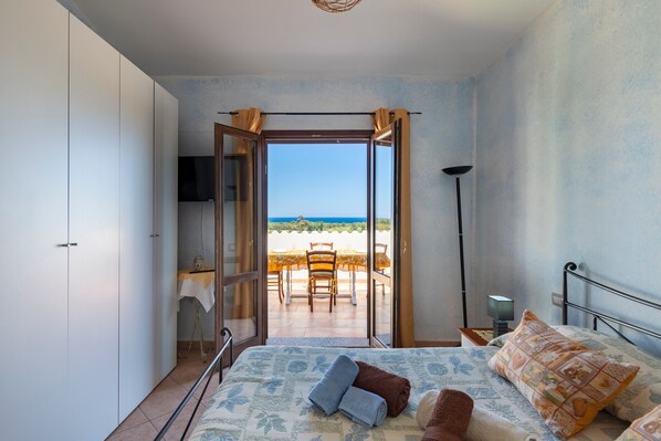 A bedroom with a bed, a view of the beach, and a balcony with a table and chairs.