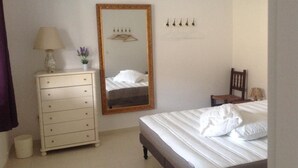 Une chambre à coucher comprenant un lit, une commode, un miroir et un luminaire fixé au mur.
