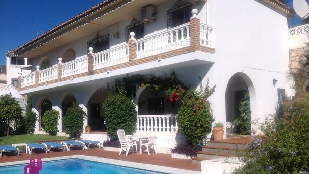 Un bâtiment à deux étages doté d’une piscine, d’un espace extérieur aménagé et d’un balcon avec des balustrades blanches.