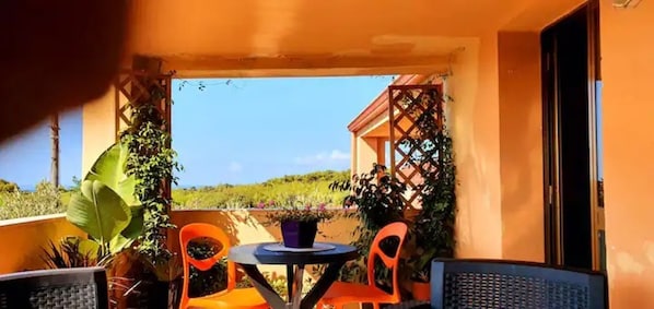 Un balcon avec deux chaises orange, une petite table ronde et des plantes en pot.
