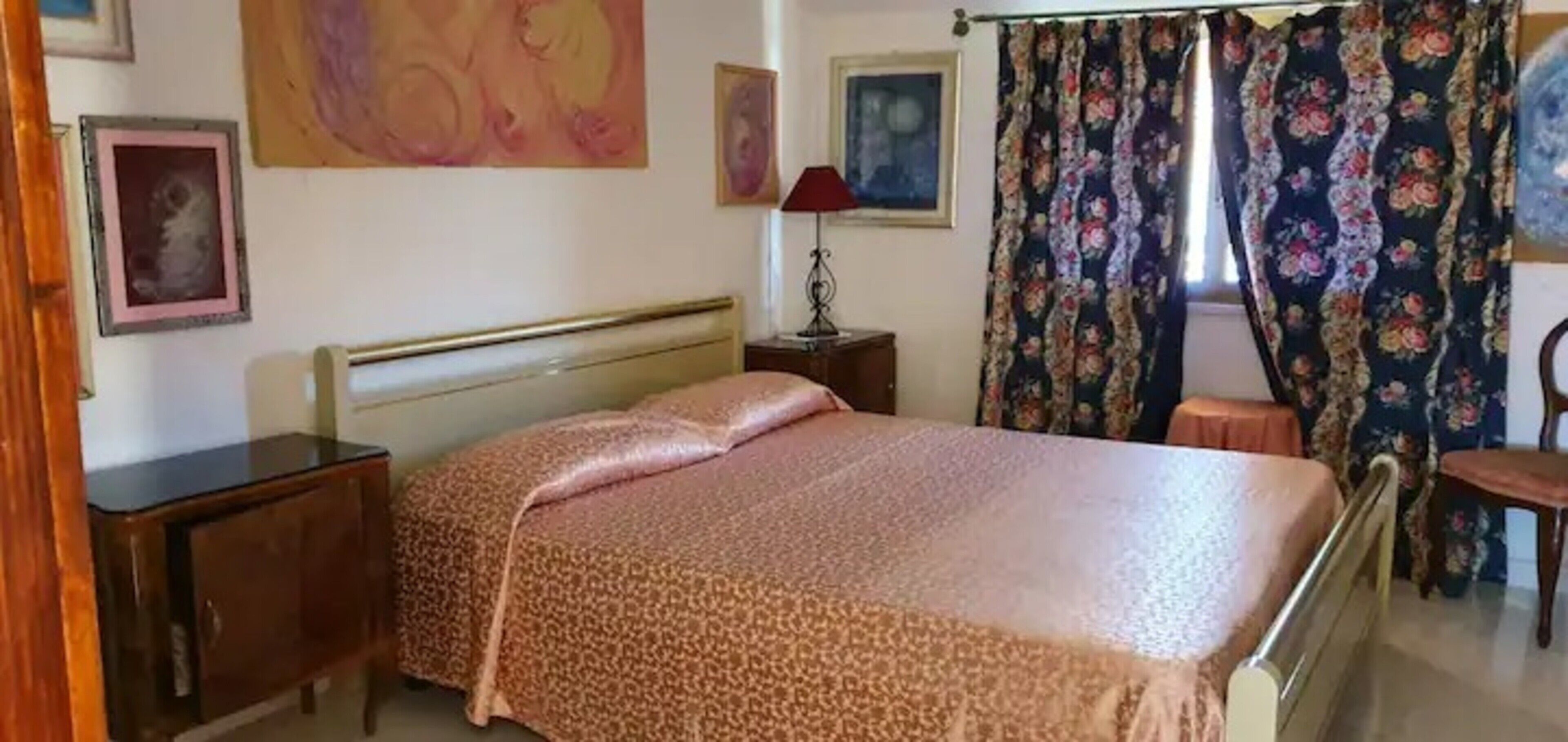 Una camera da letto con un letto, un comodino, una lampada, una sedia e tende.