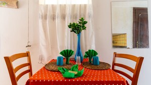 Una mesa de comedor con mantel rojo, dos sillas de madera, un florero azul con follaje verde y dos candelabros azules.
