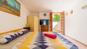 Un dormitorio con una cama, televisión, un cuadro y una escalera que da al exterior.