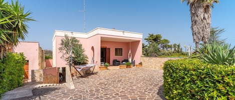 A pink building with a stone patio, outdoor seating, and a palm tree.