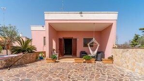 A pink building with a stone patio, outdoor seating, and a hammock. - Holiday Apartment Amare 1 close to the Beach with Covered Terrace & Garden (Torre Specchia Ruggeri)
