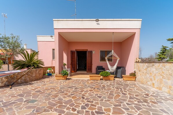 A pink building with a stone patio, outdoor seating, and a hammock.