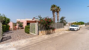 A residential street with a paved driveway, a white car parked on the side, and a pink building with a gated entrance. - Holiday Apartment Amare 1 close to the Beach with Covered Terrace & Garden (Torre Specchia Ruggeri)