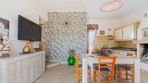 A modern kitchen with a stone backsplash, a dining area with wooden chairs, and a TV mounted on the wall. - Holiday Apartment Amare 1 close to the Beach with Covered Terrace & Garden (Torre Specchia Ruggeri)