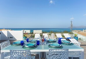 Mesa posta para refeição com vista para o mar, cadeiras brancas e céu claro.