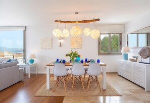 Uma sala de jantar moderna com uma mesa de madeira, cadeiras brancas e um lustre.