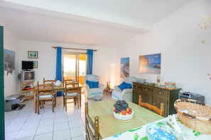 Een woonkamer met een eettafel, stoelen, een televisie en een fruitschaal.
