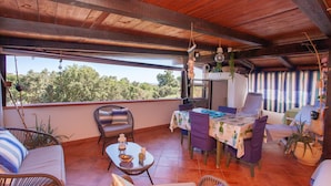 Un porche cubierto con muebles de mimbre, una mesa con mantel y vistas a árboles.