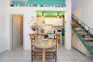 Een keuken met witte kasten, een eettafel met stoelen, een trap met groene leuningen en een plafond in teal kleur.