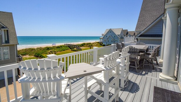 A wooden deck with white Adirondack chairs and a table, overlooking a beach and ocean. - Experience luxury at Footprints: a spacious 6-bedroom oceanfront home in North Topsail Beach. (North Topsail Beach)