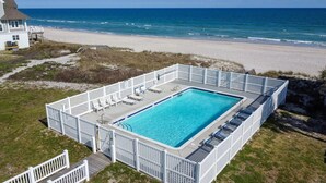 A rectangular pool with a white fence, surrounded by a grassy area and a beach view. - Experience luxury at Footprints: a spacious 6-bedroom oceanfront home in North Topsail Beach. (North Topsail Beach)