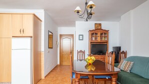 A kitchen with wooden cabinets, a dining table with chairs, a television, and a green sofa. - Apartment Nieves 2 with Sea View, Terrace & Wi-Fi (Nerja)