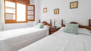 A bedroom with two beds, a nightstand, a lamp, and a window with wooden shutters. - Apartment Nieves 2 with Sea View, Terrace & Wi-Fi (Nerja)