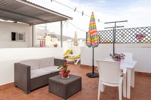 Une terrasse avec un canapé, une petite table, une chaise, un parasol et une plante en pot.