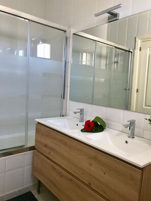 A bathroom with a glass shower enclosure, a white sink with a wooden vanity, and a mirror above the sink.