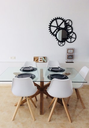 Un comedor con mesa de vidrio, sillas blancas y un adorno decorativo de ruedas en la pared.