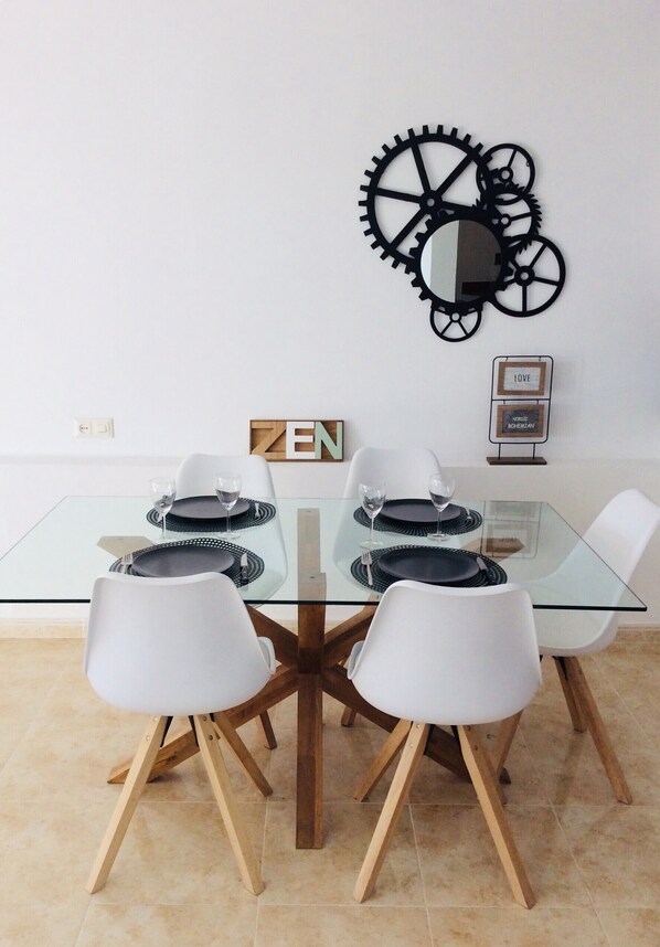 Un comedor con mesa de vidrio, sillas blancas y un adorno decorativo de ruedas en la pared.