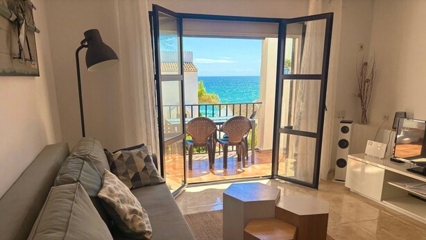 Un salon comprenant un canapé, une table basse, un téléviseur et un balcon avec vue sur la mer.