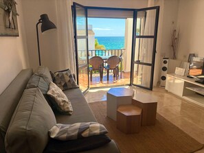 Una sala de estar con un sofá, una mesa de centro, un televisor y un balcón con vistas al mar.