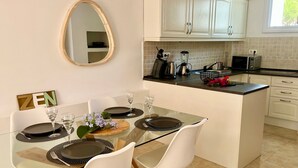 Une cuisine moderne avec des meubles blancs, une table à manger en verre et un petit îlot central doté d’un évier.