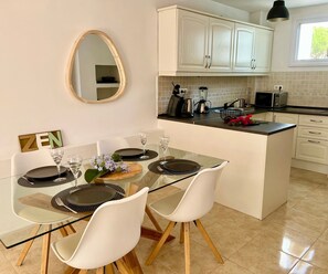 Una cocina moderna con armarios blancos, una mesa de comedor de cristal y una pequeña isla con fregadero.