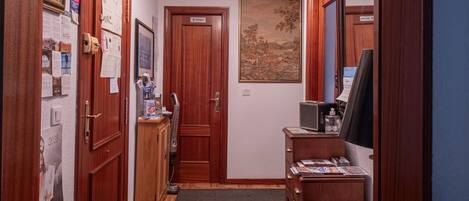 A hallway with wooden floors, a dark rug, wooden cabinets, a television, and a ceiling light.