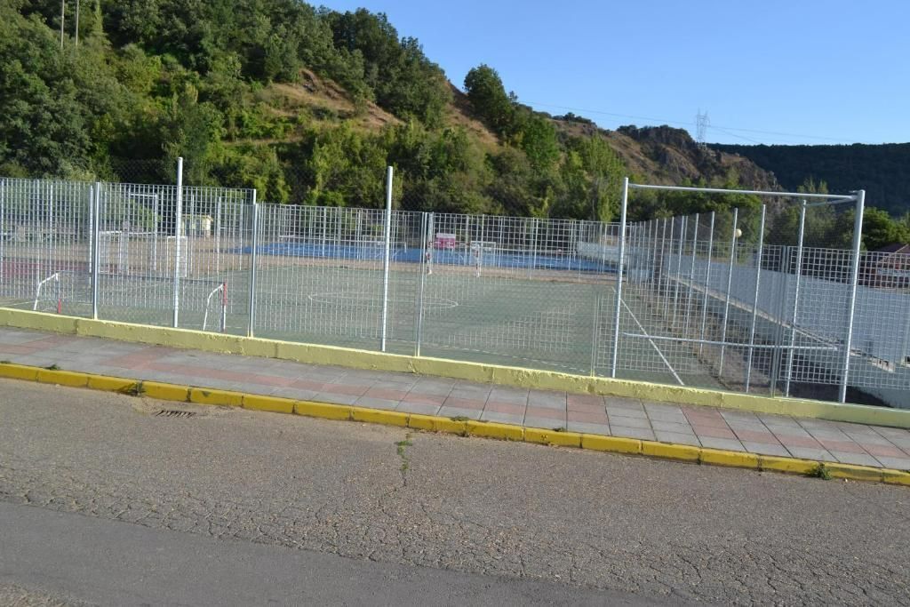 A fenced sports court with a yellow curb and a hilly landscape in the background.
