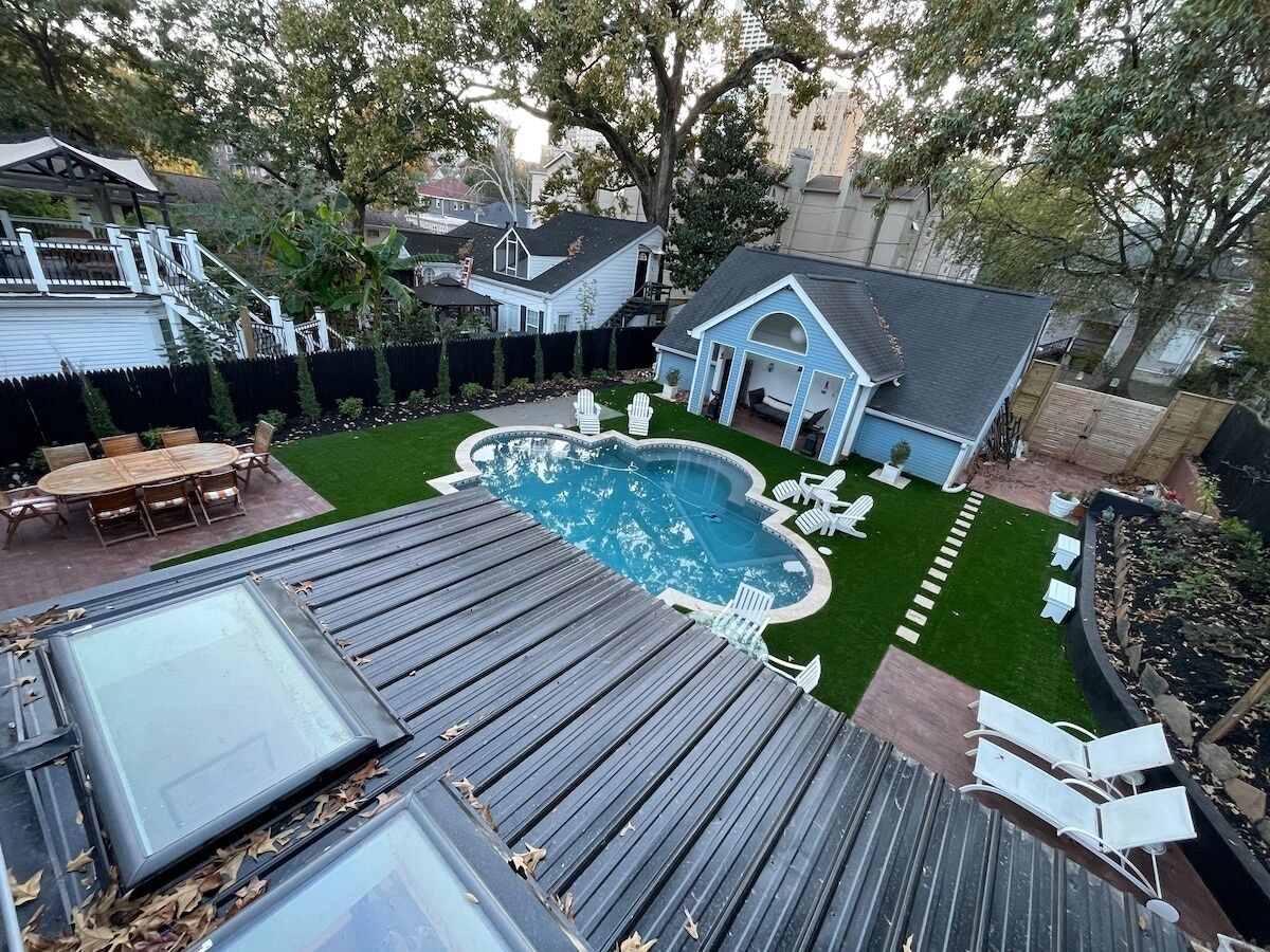Un jardin avec une piscine, une terrasse couverte et une petite maison bleue.
