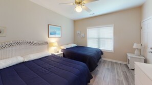 Two beds with dark blue bedspreads, ceiling fan, and lamps.