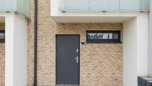A modern building facade with a dark-colored door, a small window, and a visible number '15' on the wall. - Spacious Apartment | 3 Bedrooms, Terrace, 300 m to the Beach (Rewal)