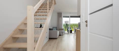A modern interior with a wooden staircase, a sofa, a dining area, and a view through a glass door.