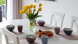 A dining table with a clear glass vase of yellow flowers, multiple bowls, and a plate of sliced watermelon and strawberries. - Spacious Apartment | 3 Bedrooms, Terrace, 300 m to the Beach (Rewal)
