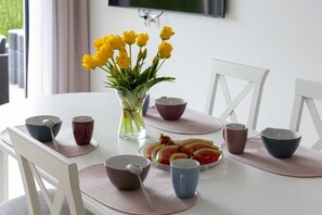 A dining table with a clear glass vase of yellow flowers, multiple bowls, and a plate of sliced watermelon and strawberries. - Spacious Apartment | 3 Bedrooms, Terrace, 300 m to the Beach (Rewal)