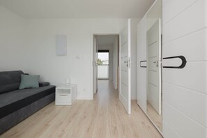 A modern, minimalistic bedroom with a grey sofa, a bedside table, and a wardrobe with sliding doors. - Spacious Apartment | 3 Bedrooms, Terrace, 300 m to the Beach (Rewal)