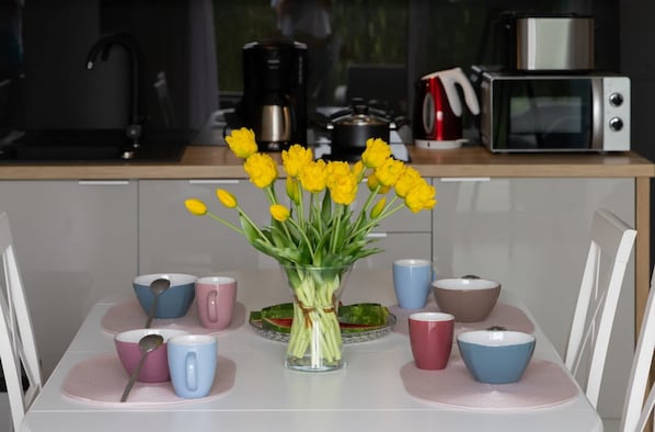 A dining table with a vase of yellow flowers, multiple cups, and a spoon.