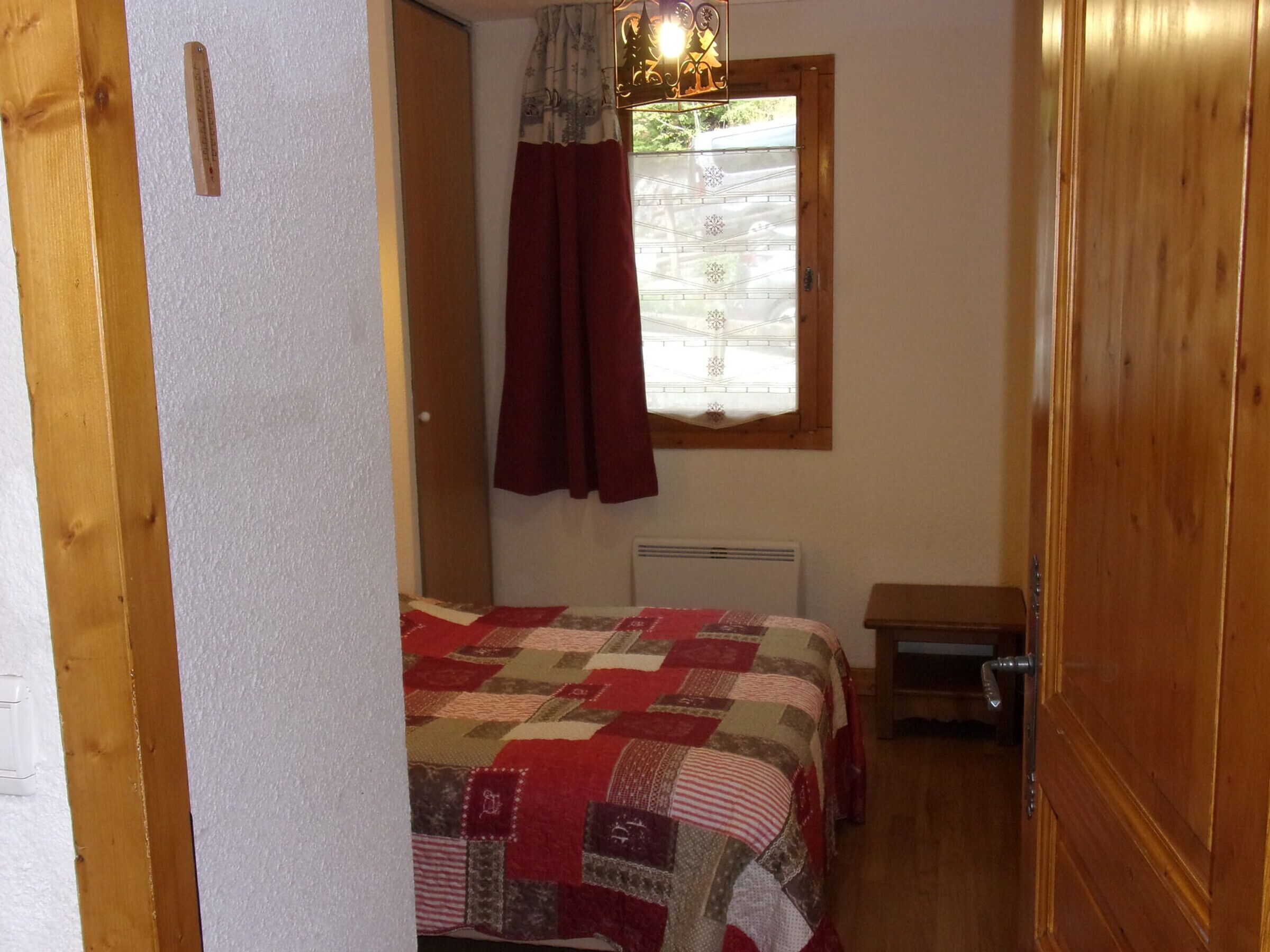 A bedroom with a wooden door, a bed with a quilt, a window with curtains, and a radiator.