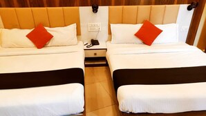 A hotel room with two beds, each with a white mattress, a brown headboard, and a red pillow. There is a nightstand between the beds with a phone and a power outlet. - Hotel Keerthana Inn (Puttur)