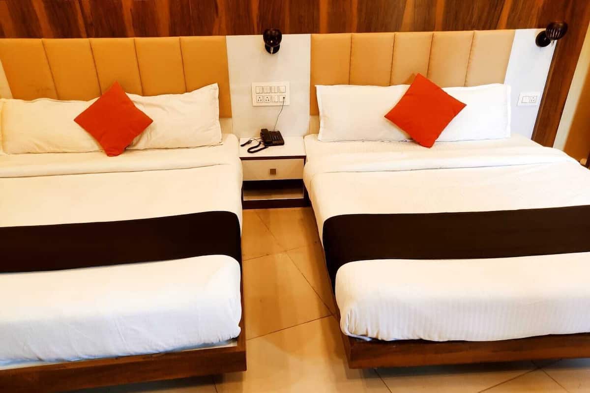 Duas camas juntas com roupa de cama branca e almofadas vermelhas, uma mesa de cabeceira com um telefone e uma tomada na parede.