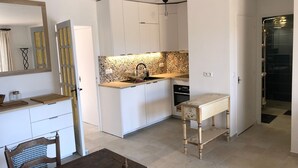 Una cocina compacta con armarios blancos, un salpicadero decorativo y una pequeña zona de comedor con una mesa y sillas de madera.