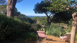 Un jardín con dos sillas rosas, un árbol grande y vista al mar.