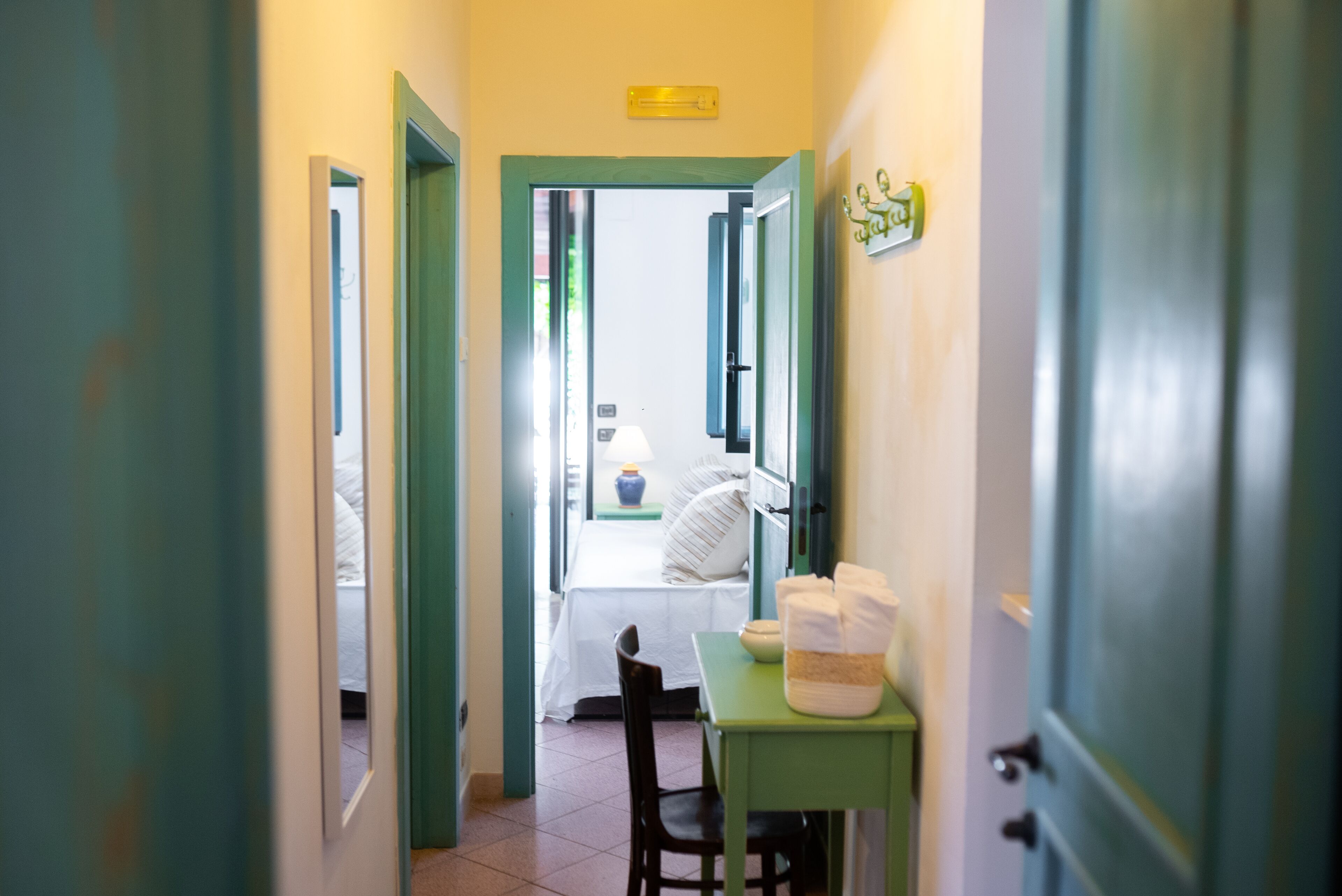 A hallway leading to a bedroom with a bed, a nightstand, and a table with towels.