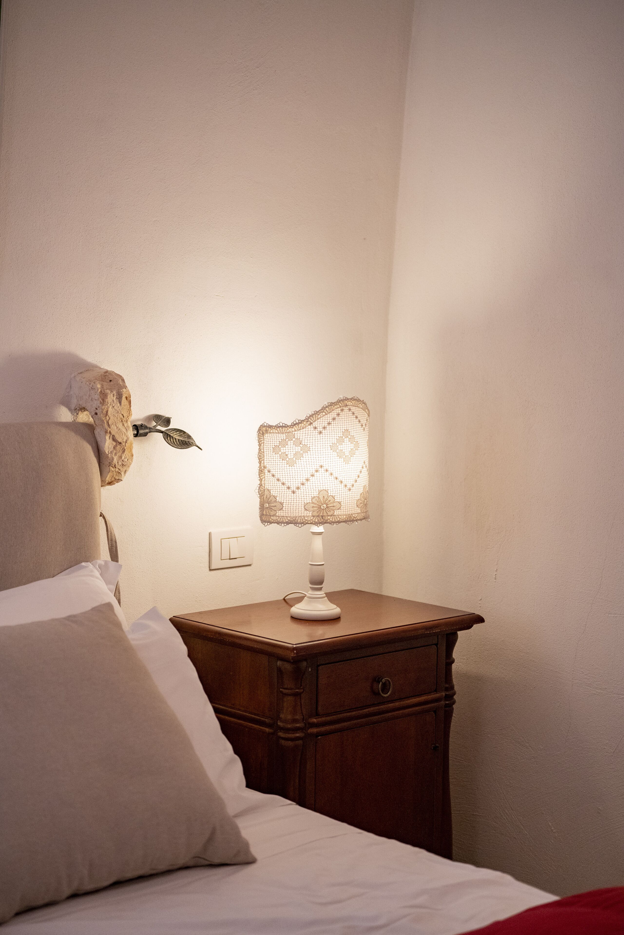 A neatly made bed with a pillow, a bedside table with a lamp, and a wall-mounted decorative item.