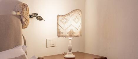 A neatly made bed with a pillow, a bedside table with a lamp, and a wall-mounted decorative item.