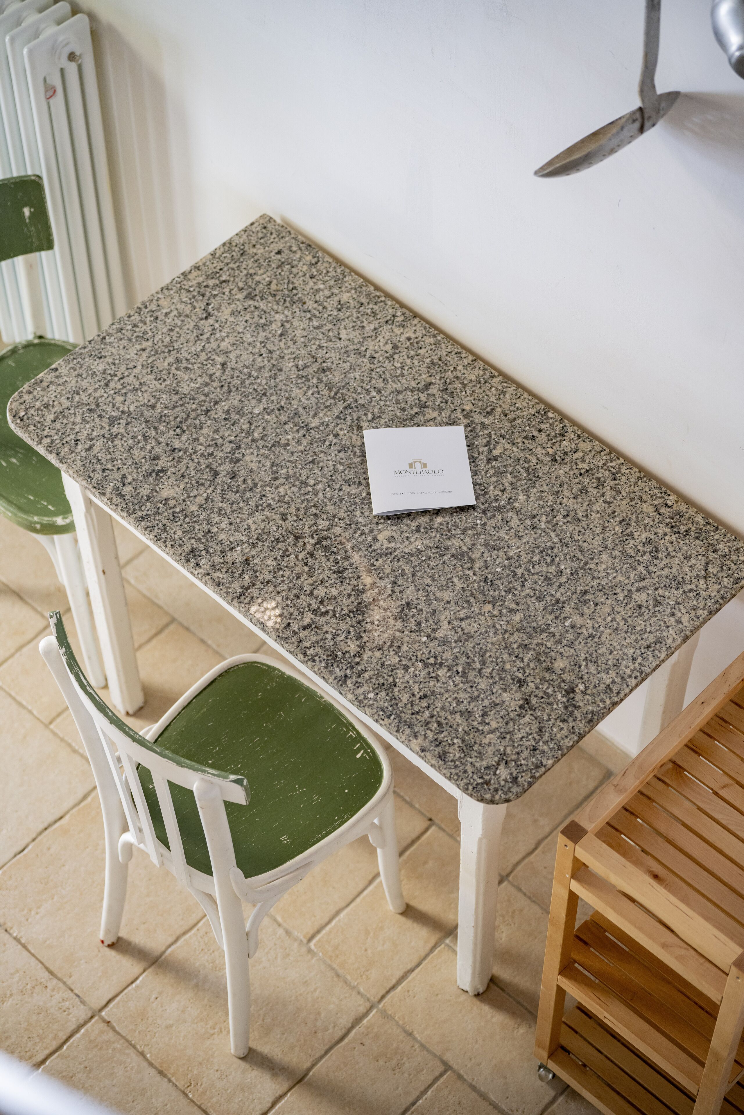 Ein kleiner Esstisch mit Granitplatte, zwei weiße Stühle mit grünen Kissen und ein kleiner Holznachttisch.